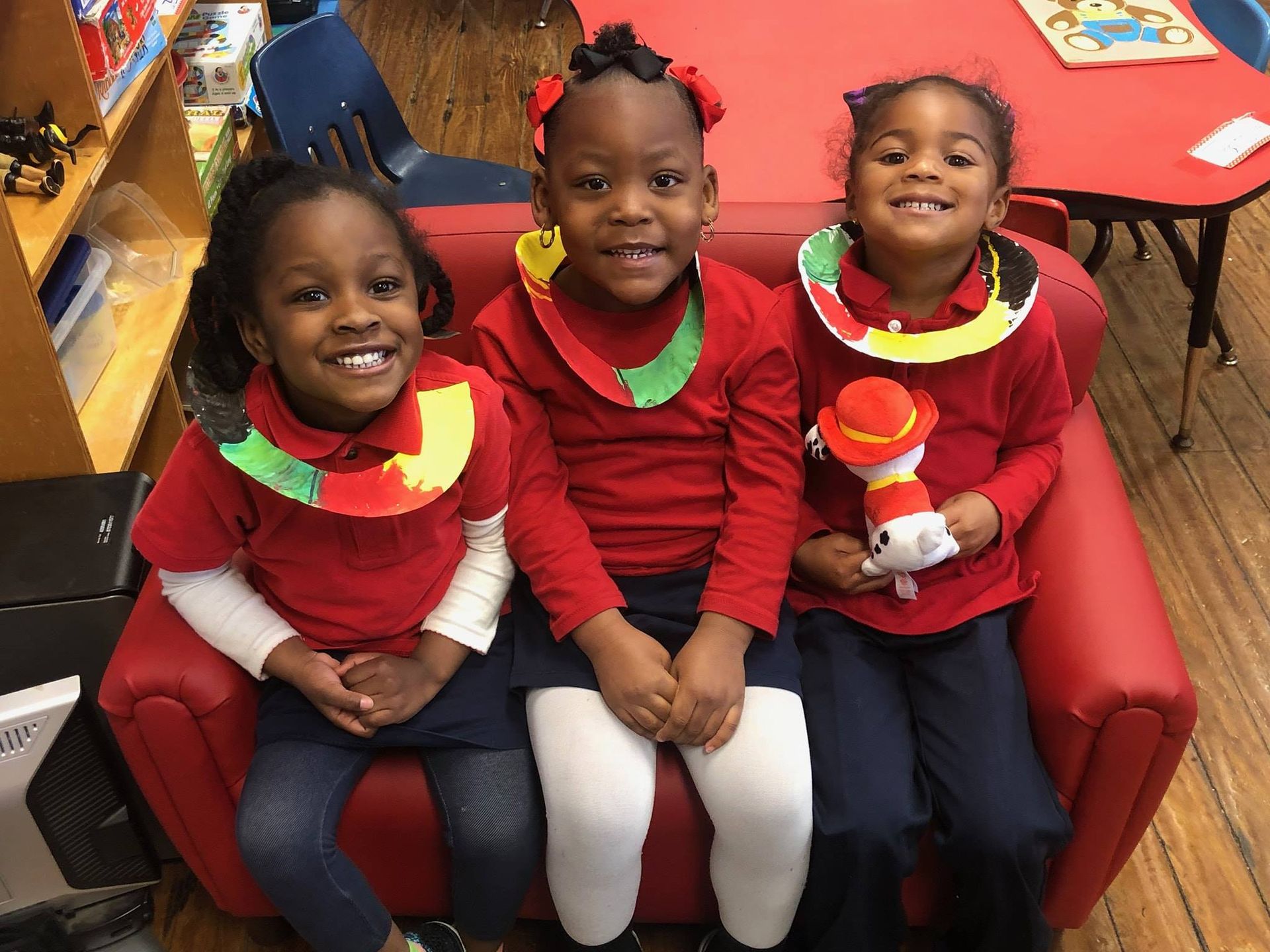 three young girls wearing red shirts are sitting on a red couch .