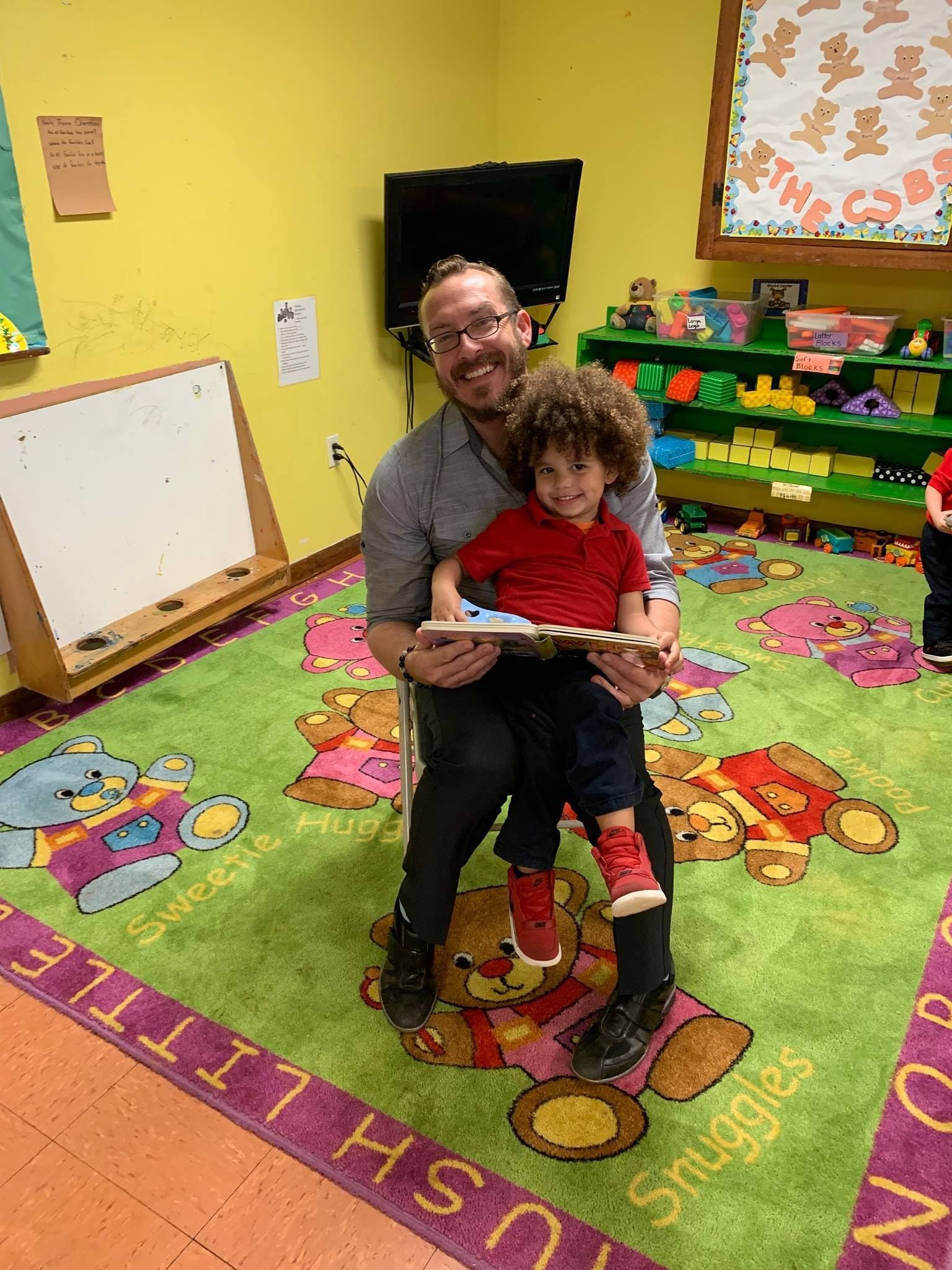 a man is sitting on a rug reading a book to a child .