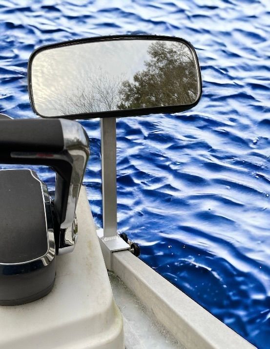 Boat mirror reflecting water beside a black seat and white railing