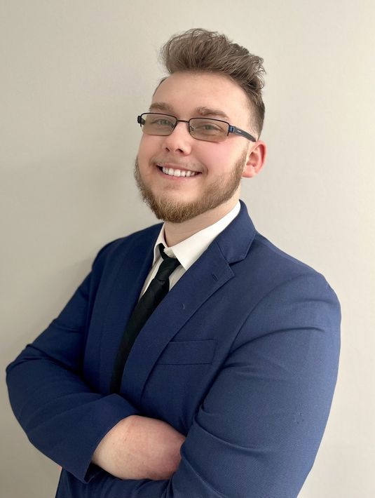 A man with a beard and glasses is wearing a blue suit and tie.
