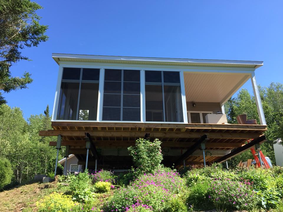 Une maison avec un porche grillagé est située au sommet d'une colline entourée d'arbres.
