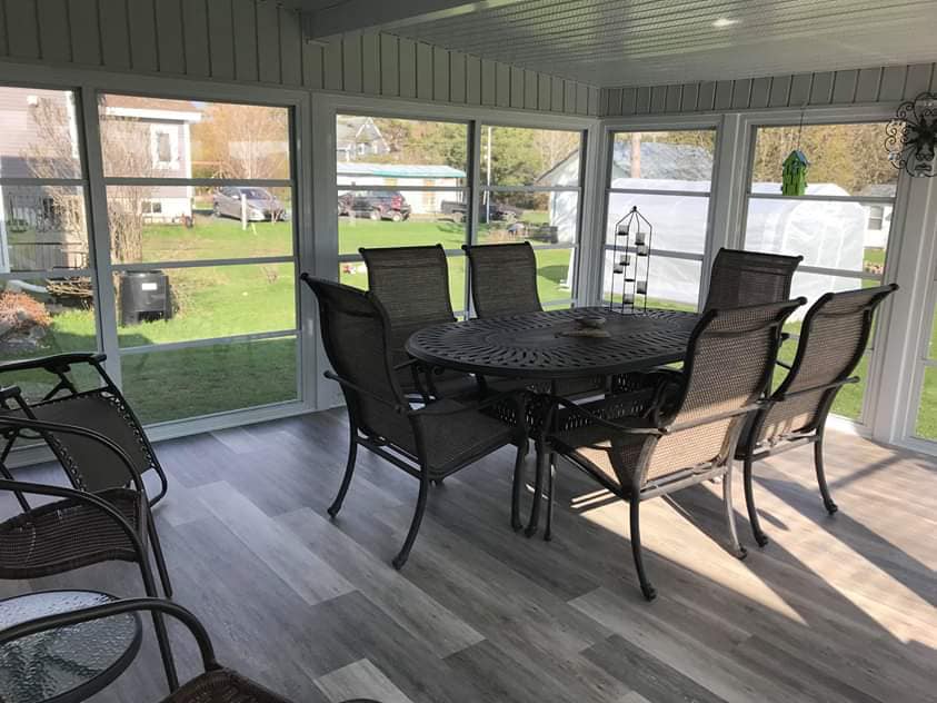 Une véranda avec une table et des chaises et beaucoup de fenêtres.