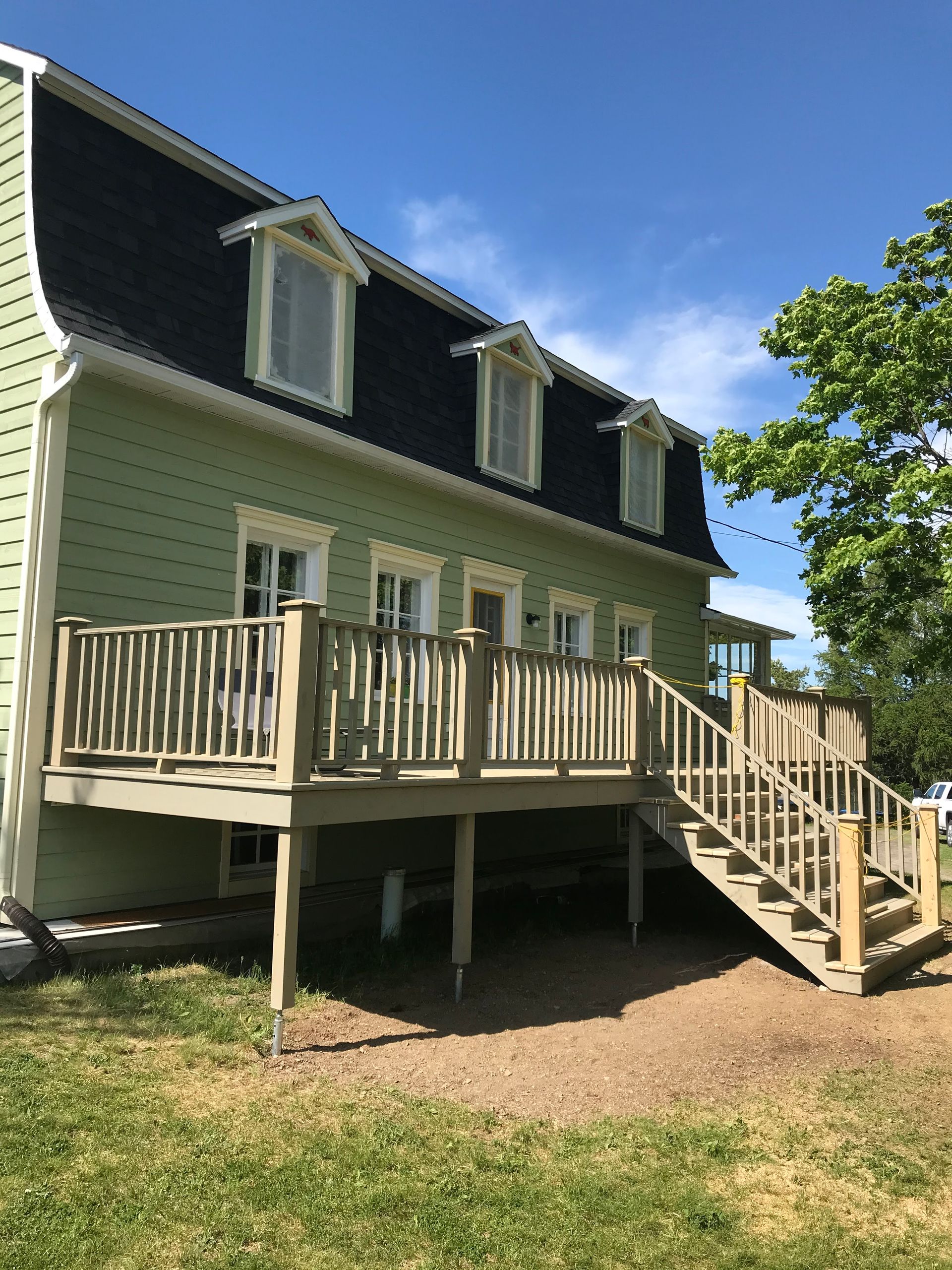Une maison verte avec une terrasse en bois et des escaliers
