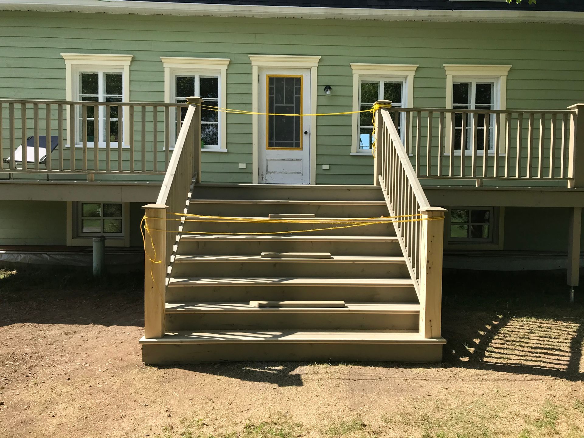 Une maison verte avec une terrasse en bois et des escaliers
