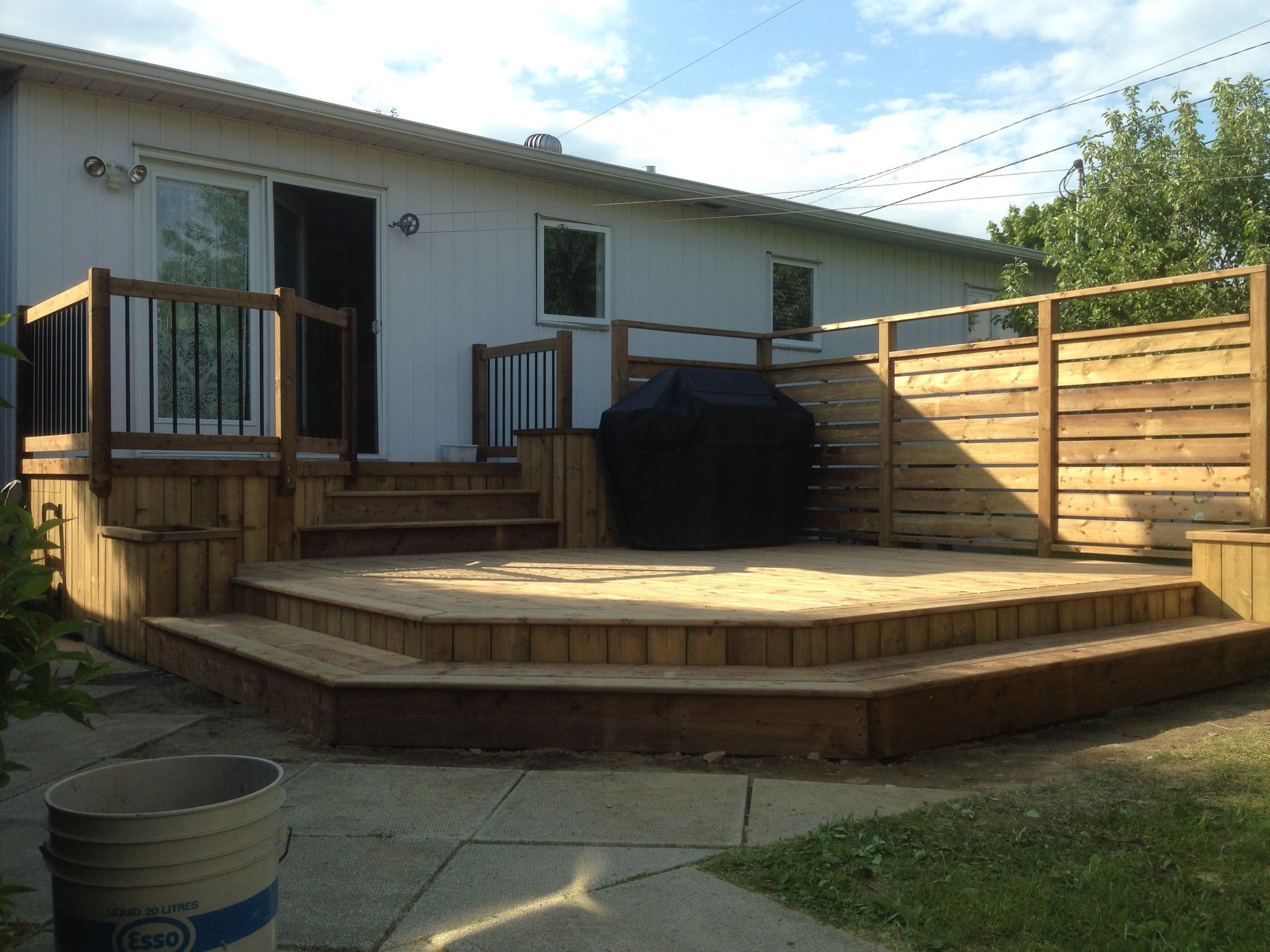 Une terrasse en bois avec des escaliers et un barbecue devant une maison.
