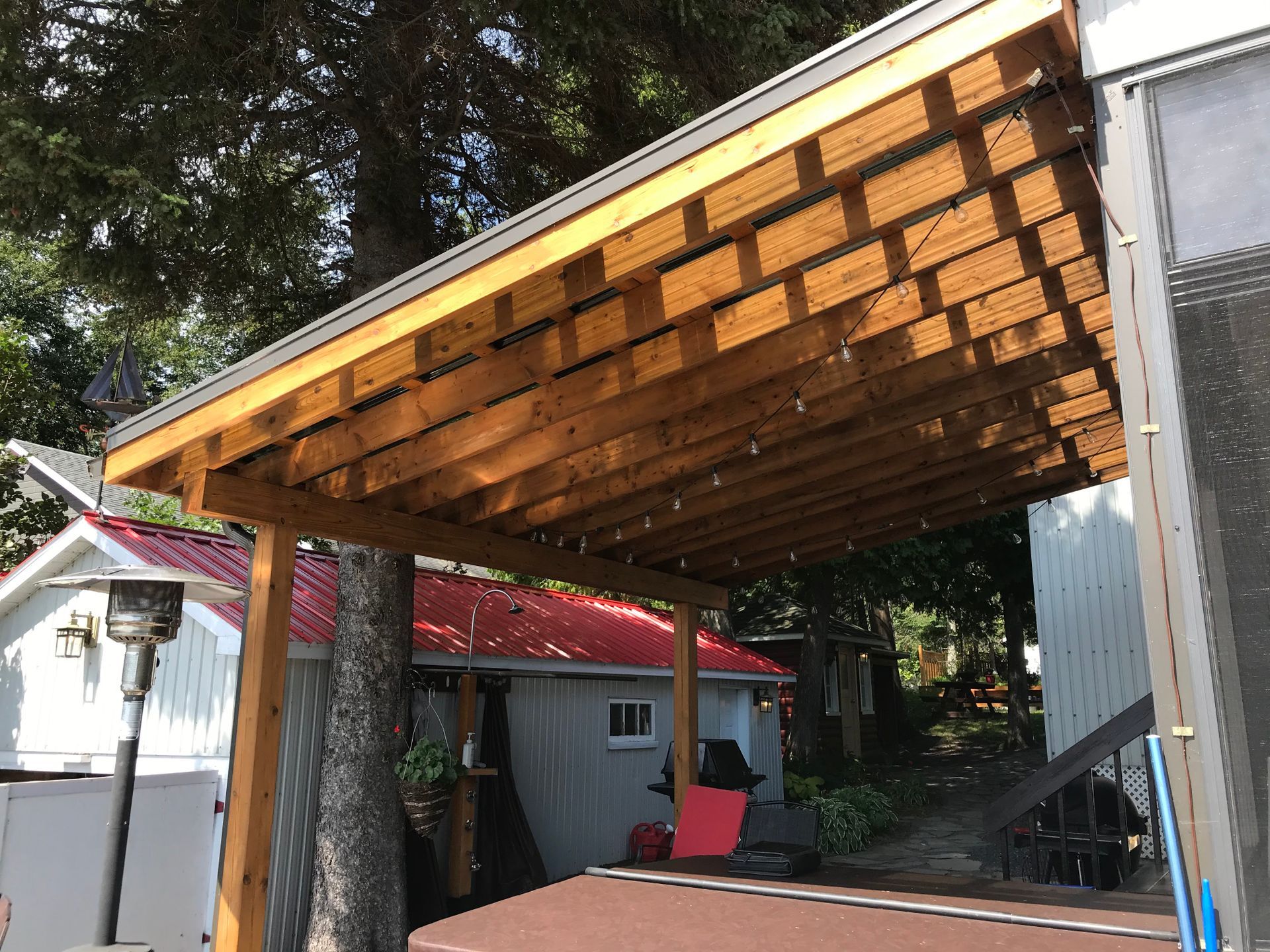 Une pergola en bois avec un toit rouge et une maison blanche en arrière-plan