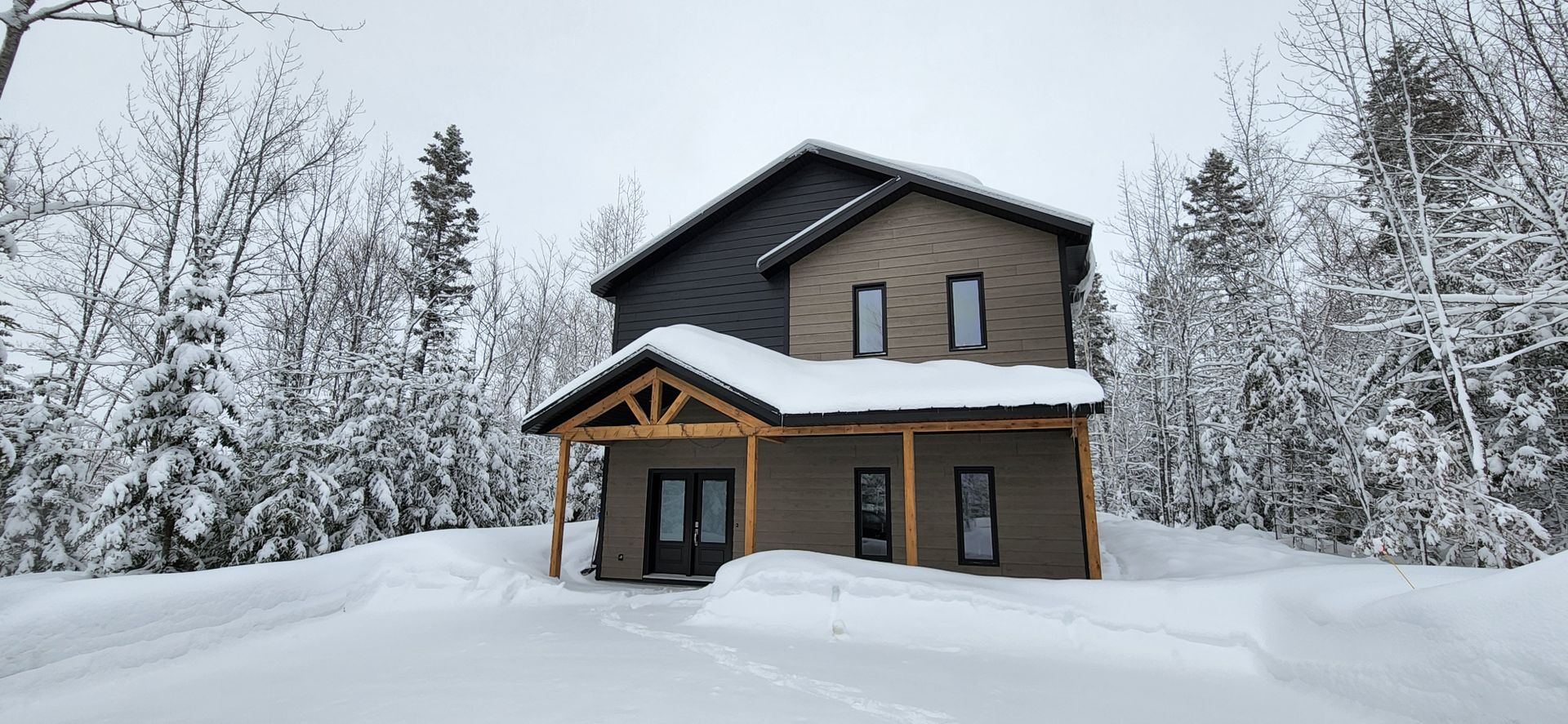 Une maison est recouverte de neige au milieu d'une forêt enneigée.