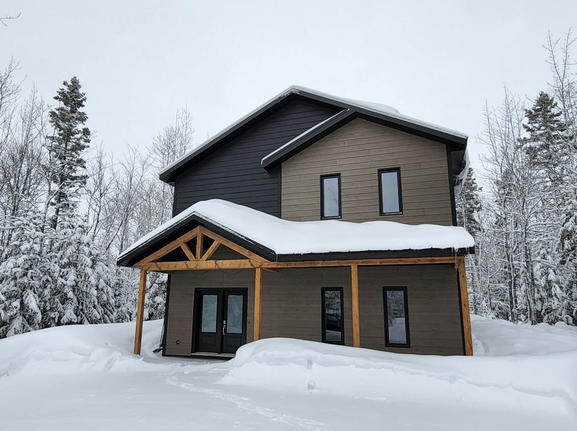 Une maison est recouverte de neige au milieu d'une forêt enneigée.