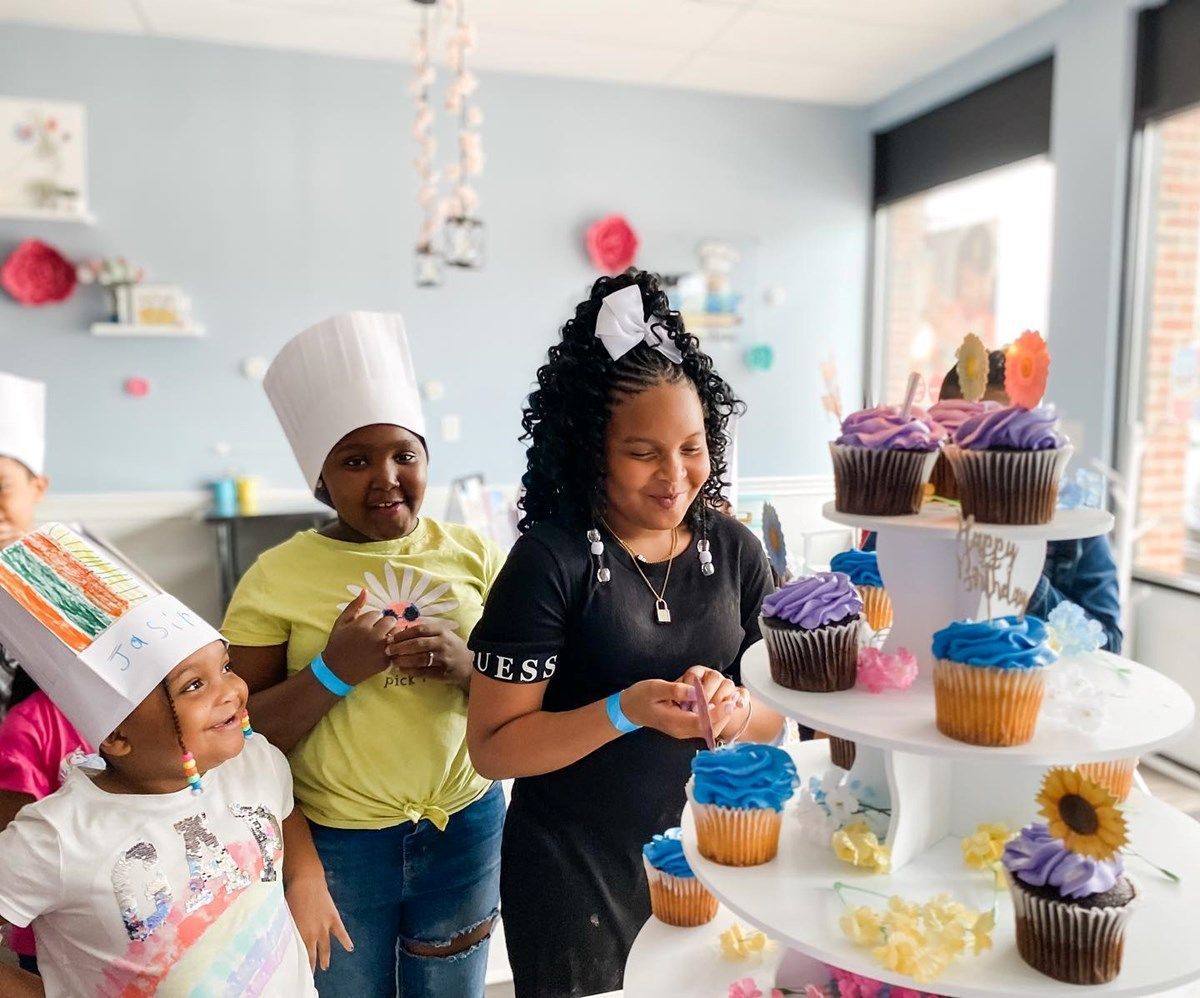 a group of young girls are standing around a cupcake display .