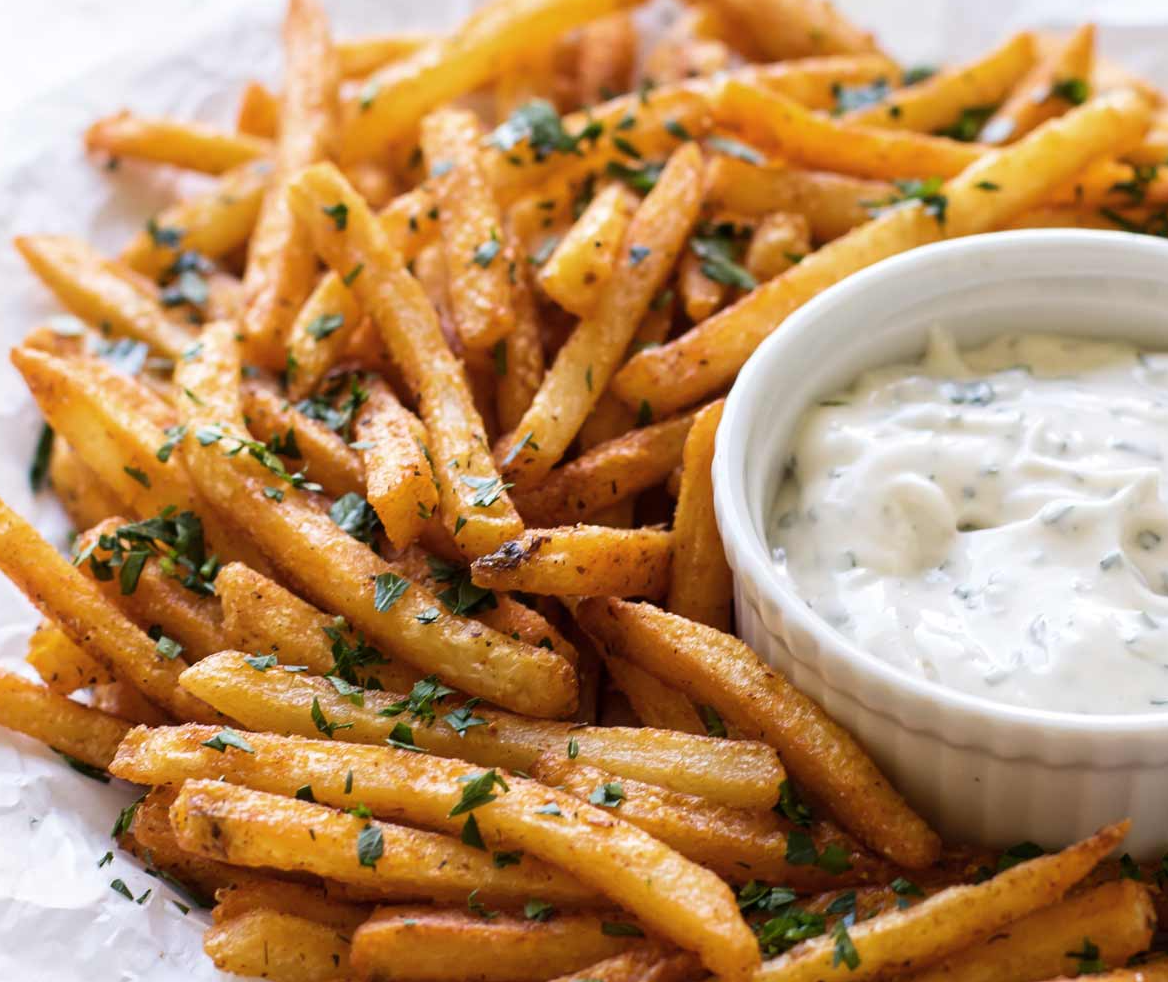 A plate of french fries with a bowl of dipping sauce.