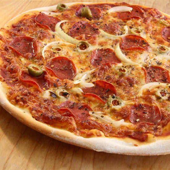 A pepperoni pizza with onions and olives on a wooden table.