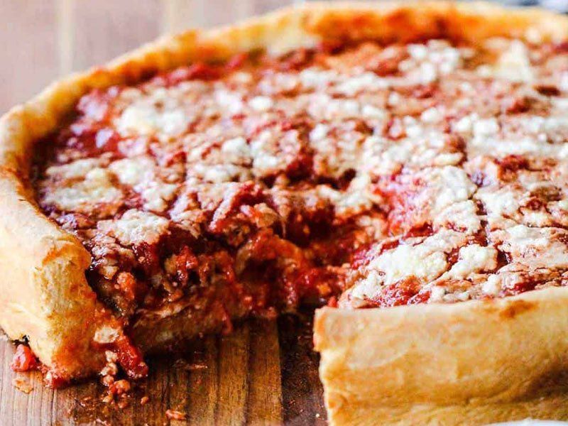 A pizza with a slice taken out of it is sitting on a wooden table.