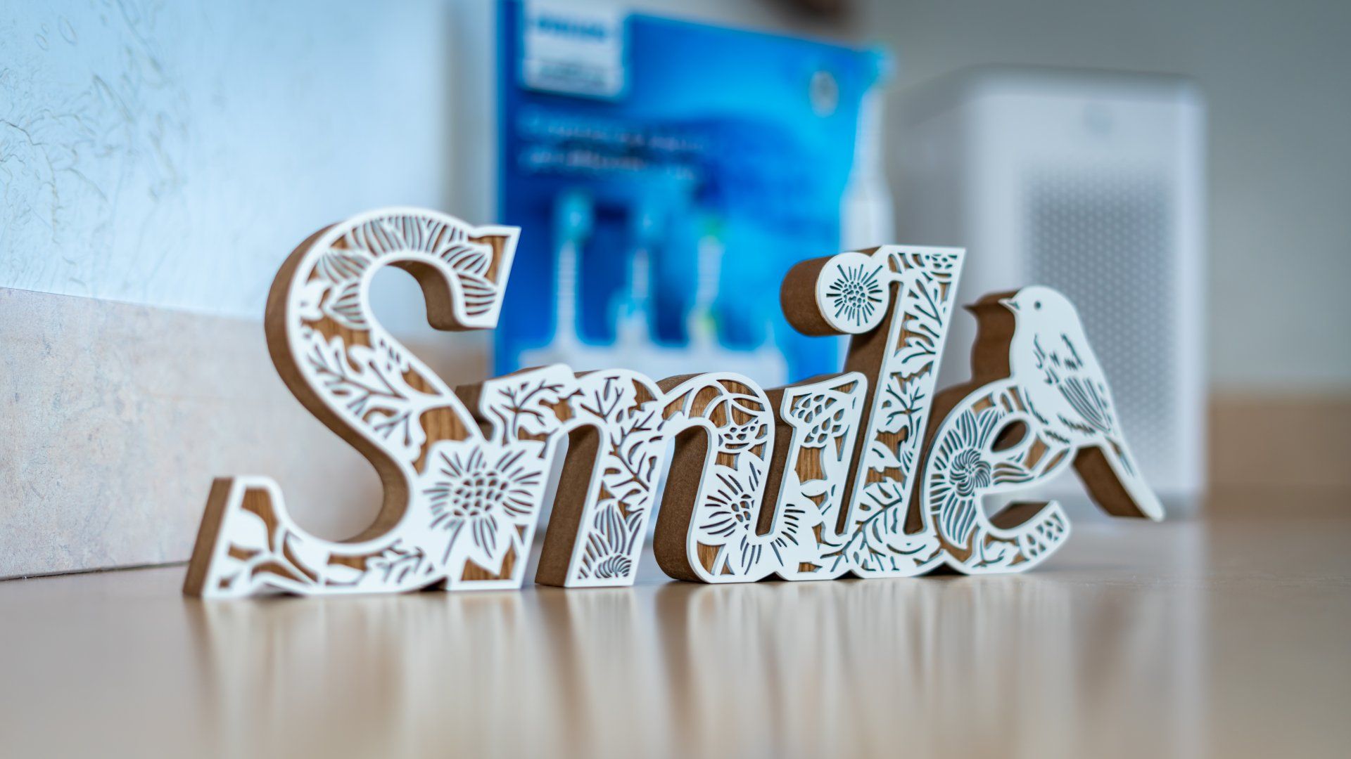 A wooden sign that says smile is sitting on a wooden table.