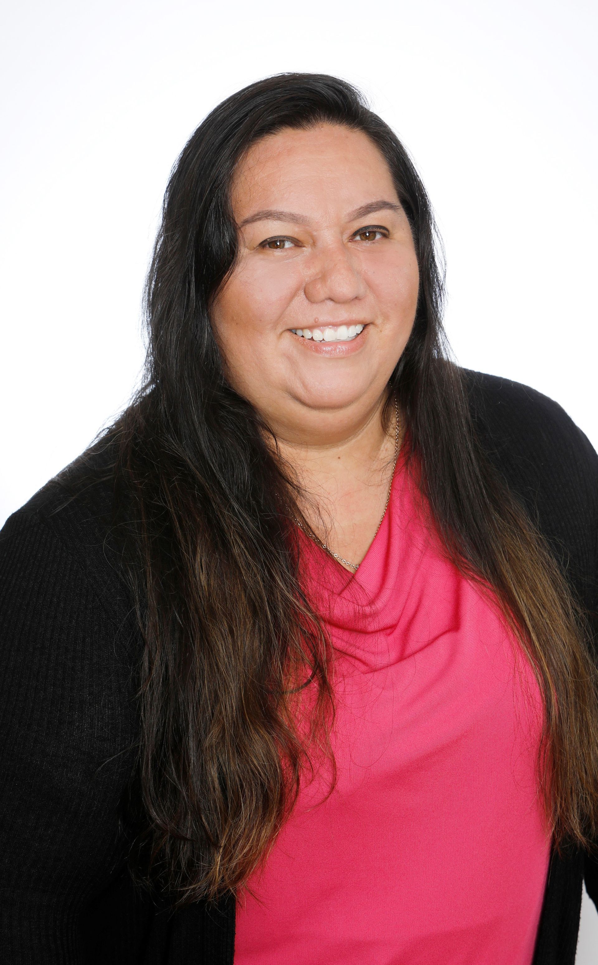 A woman with long hair is wearing a pink shirt and a black sweater.