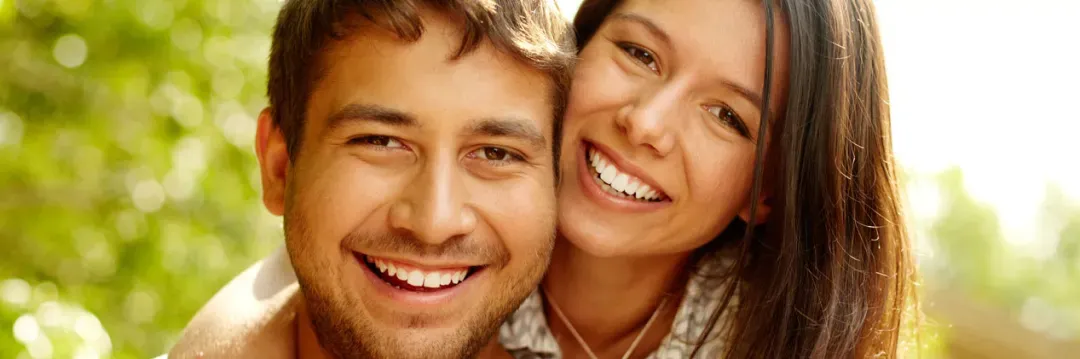 A man is giving a woman a piggyback ride and they are smiling for the camera.