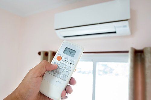 Holding a remote of an air conditioner — Electrical & Fire Services in Darwin, NT
