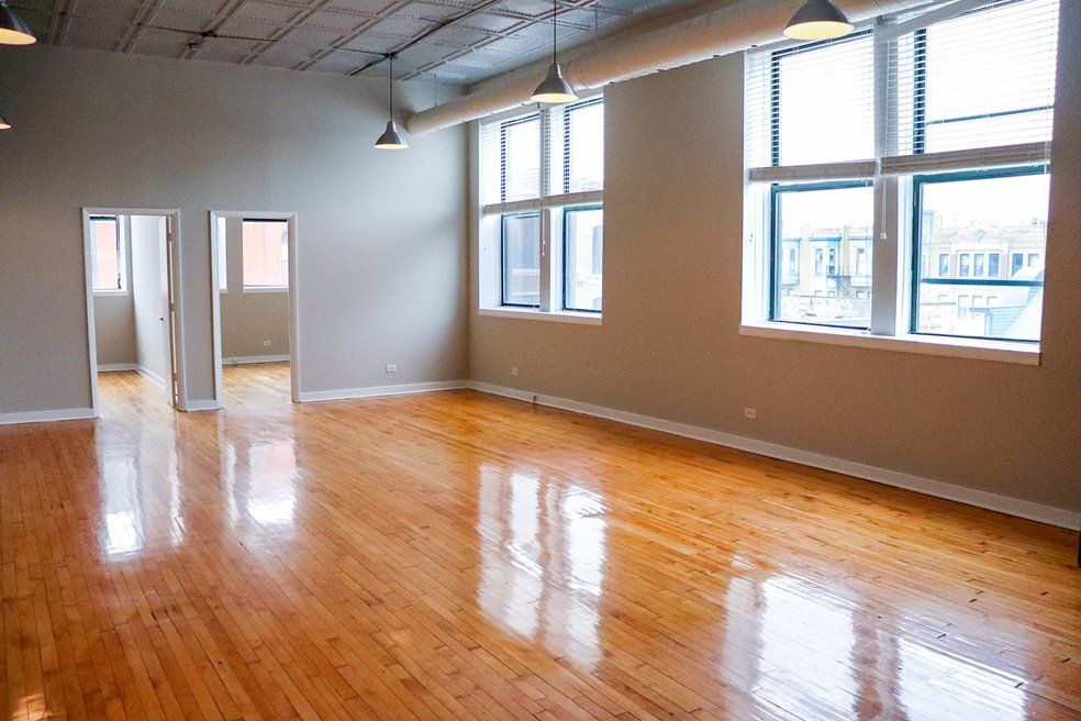 A large empty room with hardwood floors and lots of windows at 1471 N Milwaukee Apartments.