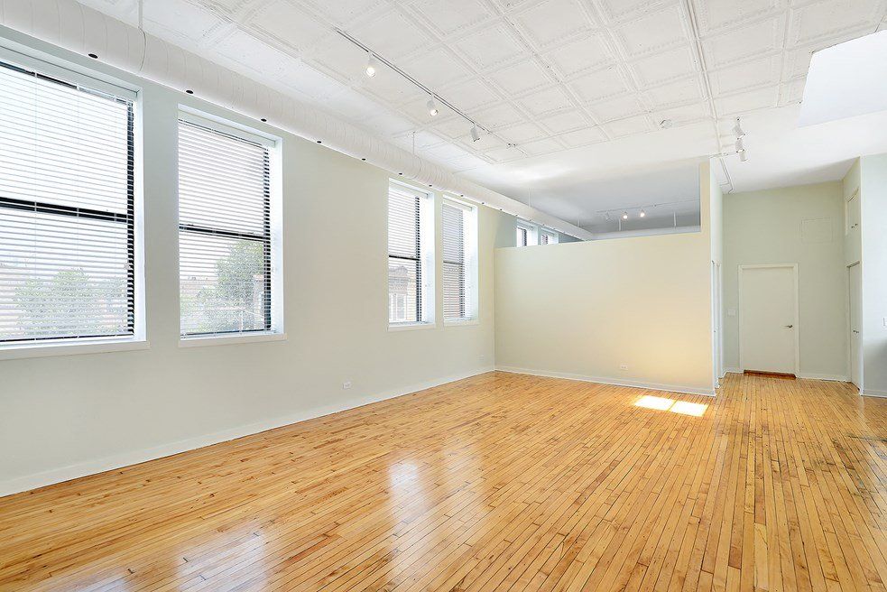 A large empty room with hardwood floors and lots of windows at 1471 N Milwaukee Apartments.