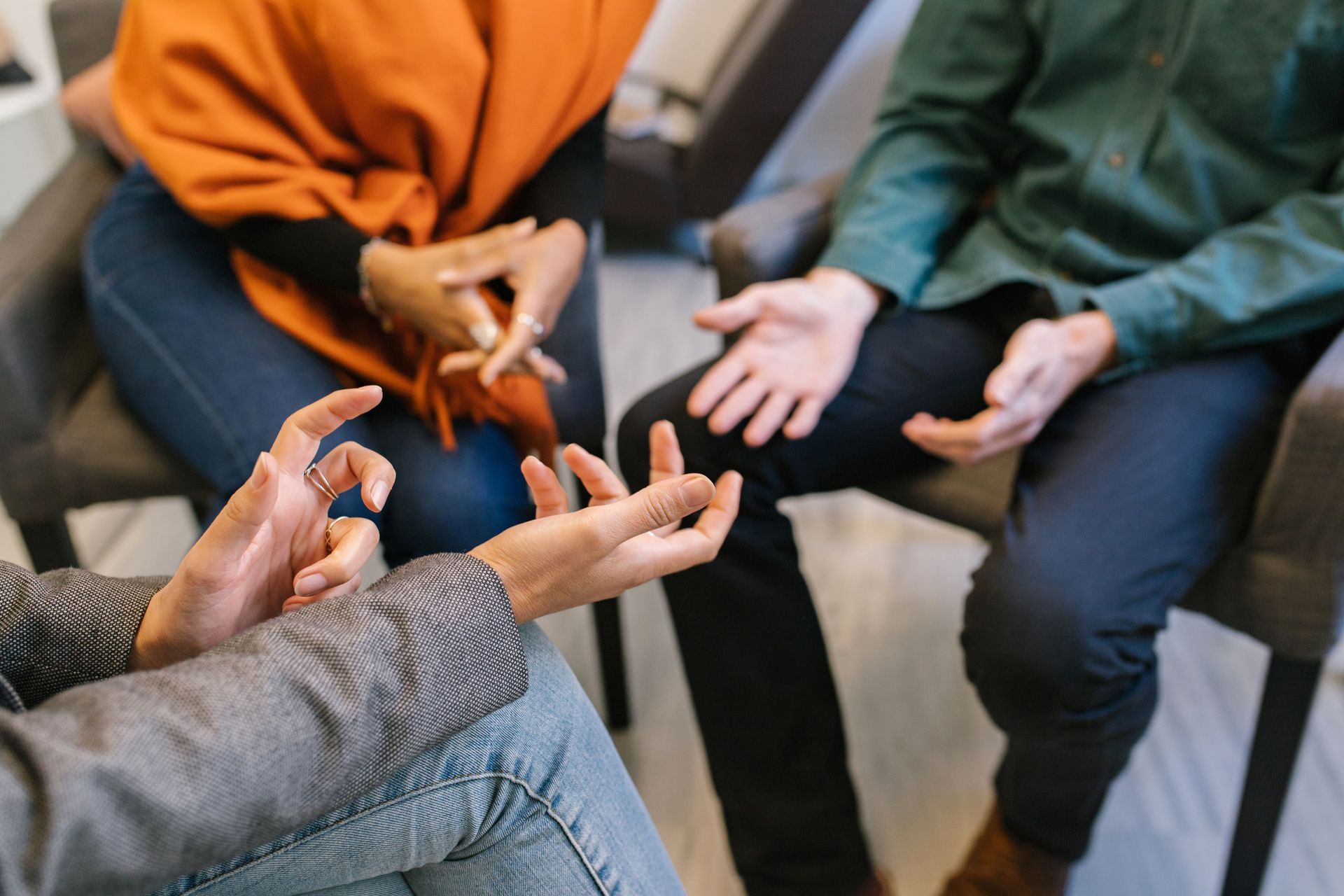 Three people in a group therapy session; hands gesturing, seated in chairs.