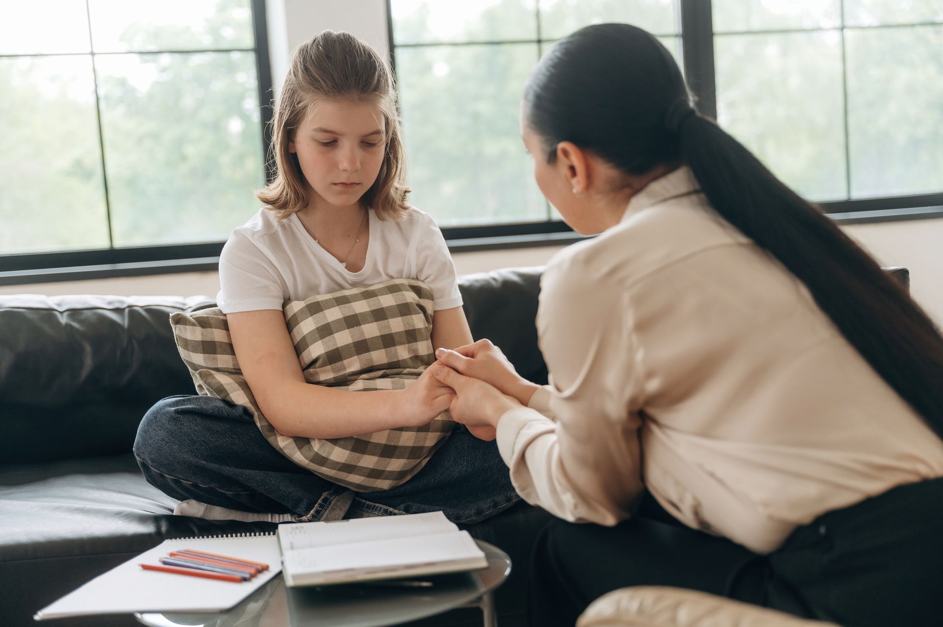Woman comforting a person holding a pillow, sitting on a couch. The person looks sad.