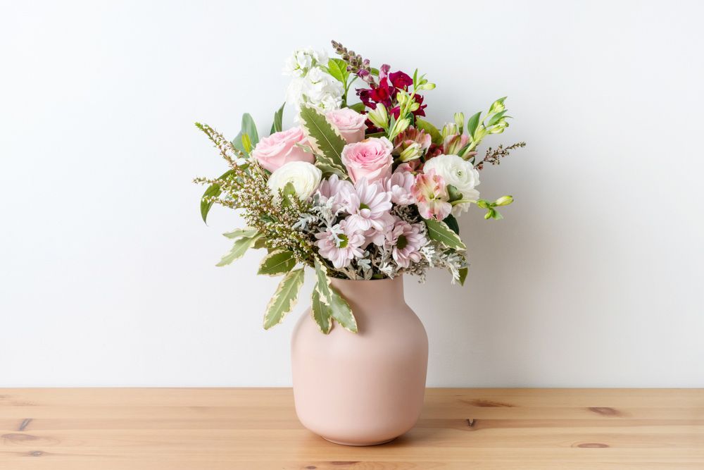 A Pink Vase Filled with Flowers Is Sitting on A Wooden Table — Pick-A-Bunch Florists & Gifts In Koumala, QLD