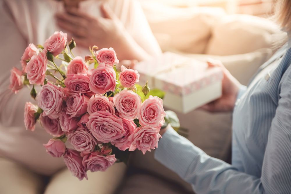 A Woman Is Holding a Bouquet of Pink Roses and A Gift Box — Pick-A-Bunch Florists & Gifts In Alligator Creek, QLD