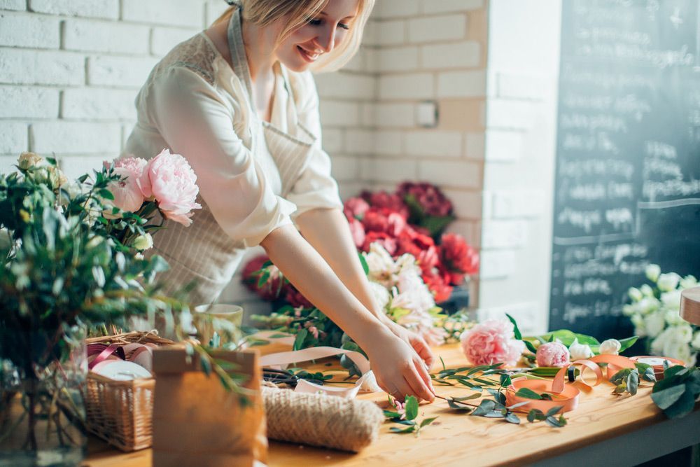 A Woman Is Arranging Flowers on A Wooden Table — Pick-A-Bunch Florists & Gifts In Armstrong Beach, QLD