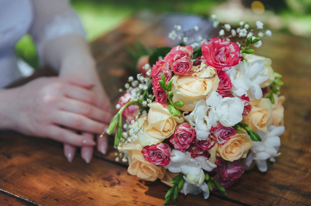 A Woman Is Holding a Bouquet of Flowers on A Wooden Table — Pick-A-Bunch Florists & Gifts In Hay Point, QLD