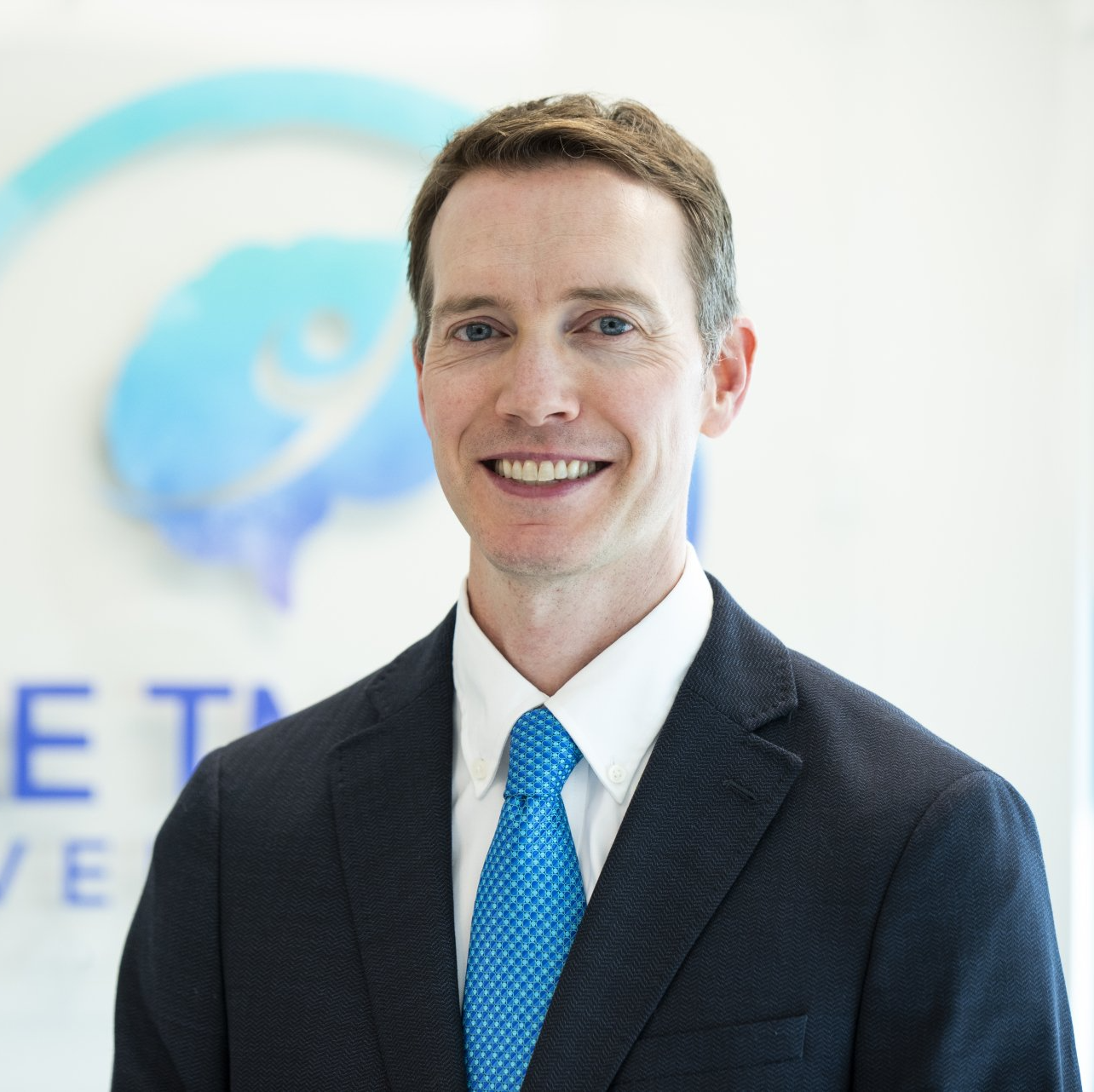 A man in a suit and tie is smiling in front of a sign that says et
