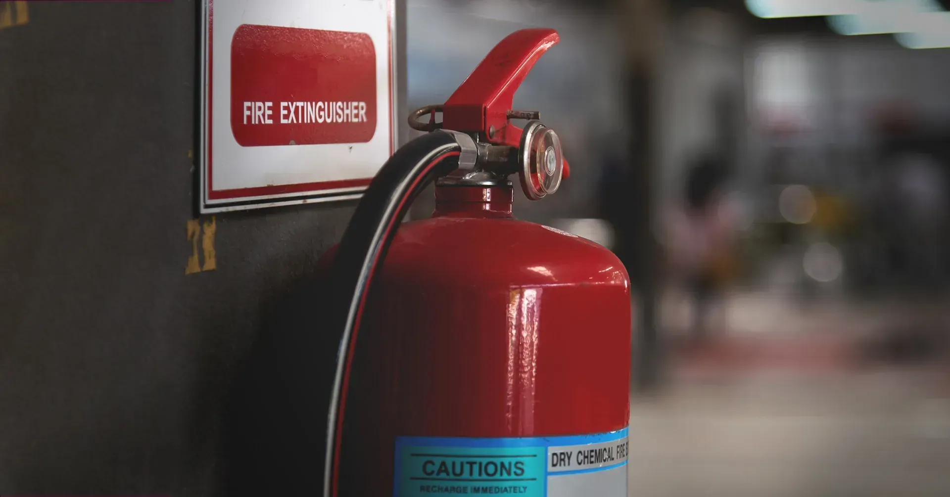 A bright red fire extinguisher mounted on a wall next to a white sign with red lettering.