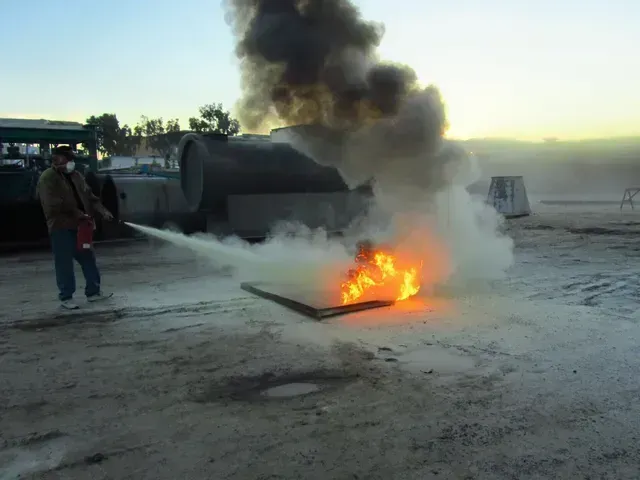 A person using a fire extinguisher to put out a small fire on the ground outdoors.