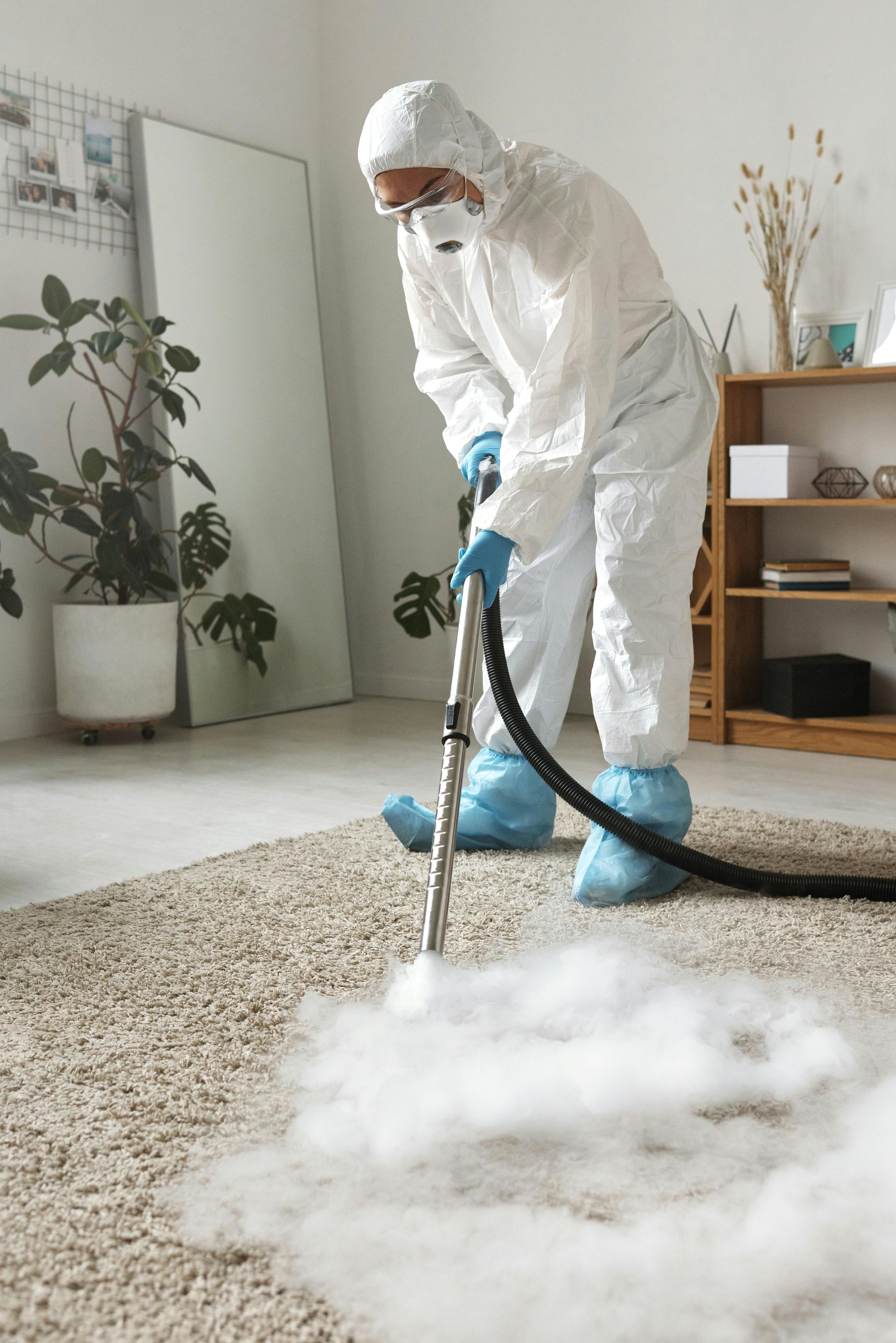 Person in protective suit vacuuming white dust from a carpet in a living room
