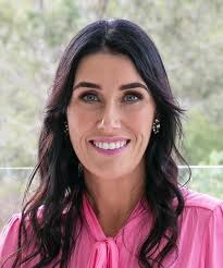 A woman in a pink shirt and tie is smiling for the camera.