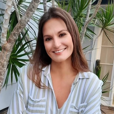 A woman in a striped shirt is smiling in front of a palm tree.