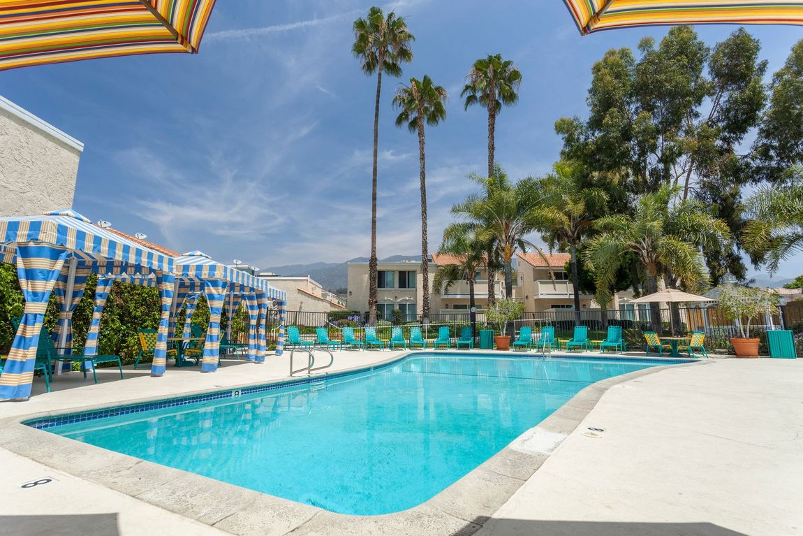 A large swimming pool surrounded by palm trees and umbrellas.
