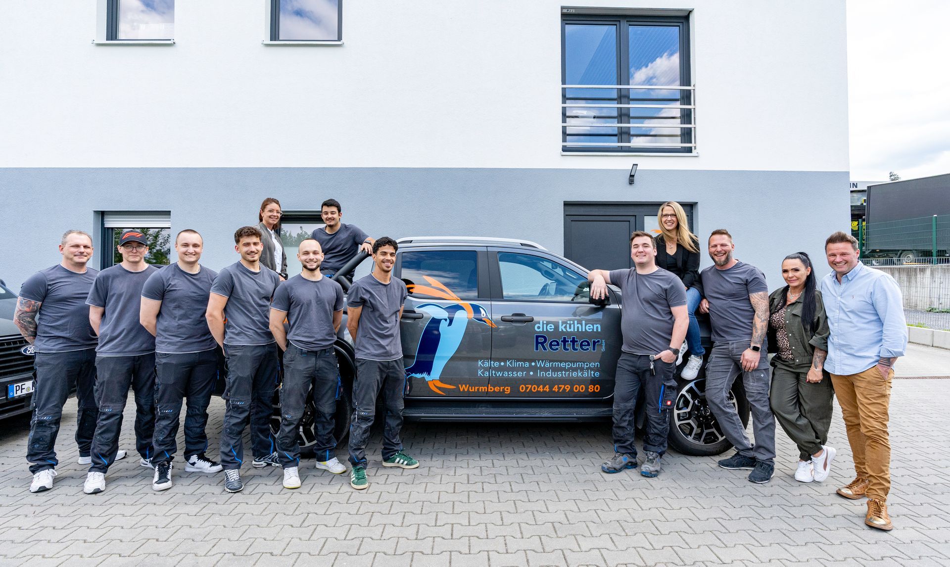 Eine Gruppe von Menschen posiert vor einem Auto für ein Foto.