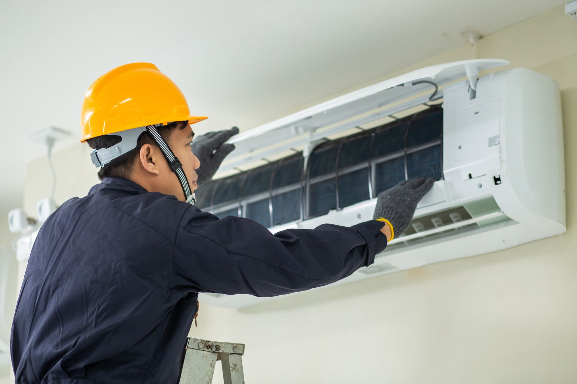 A man is working on an air conditioner on a ladder.