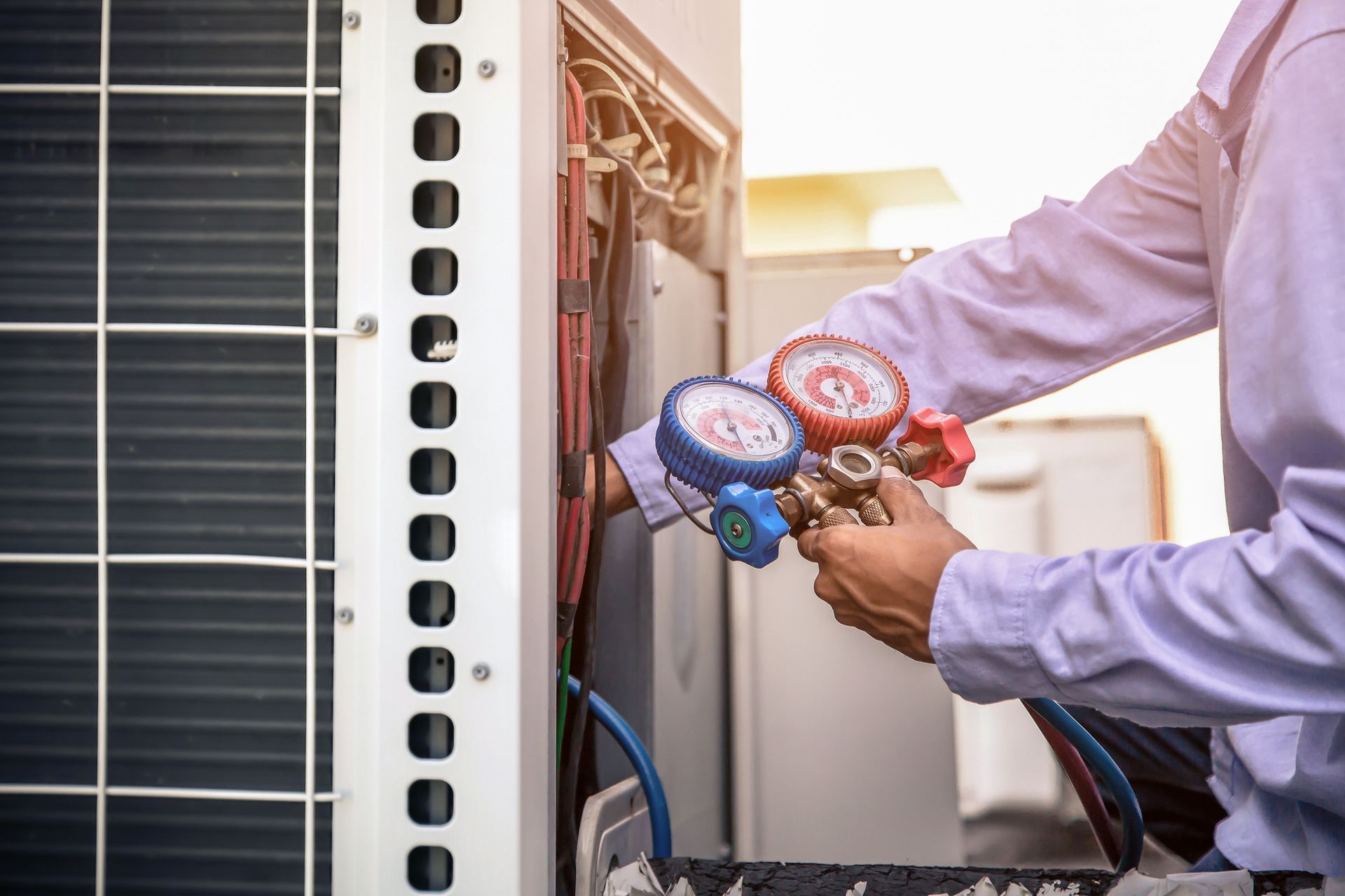 A man is working on an air conditioner with a couple of gauges.