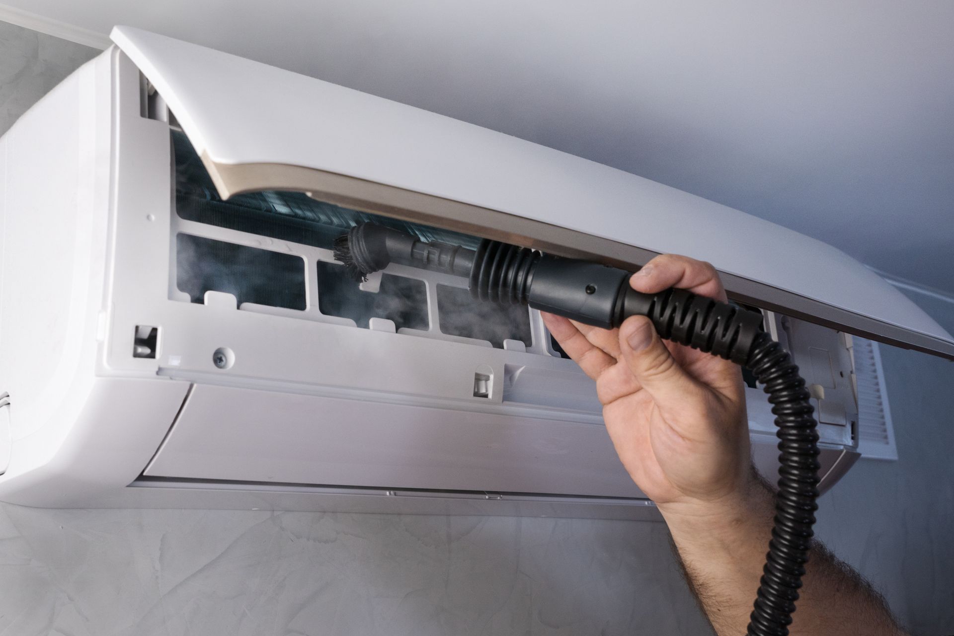 A person is cleaning an air conditioner with a vacuum cleaner.