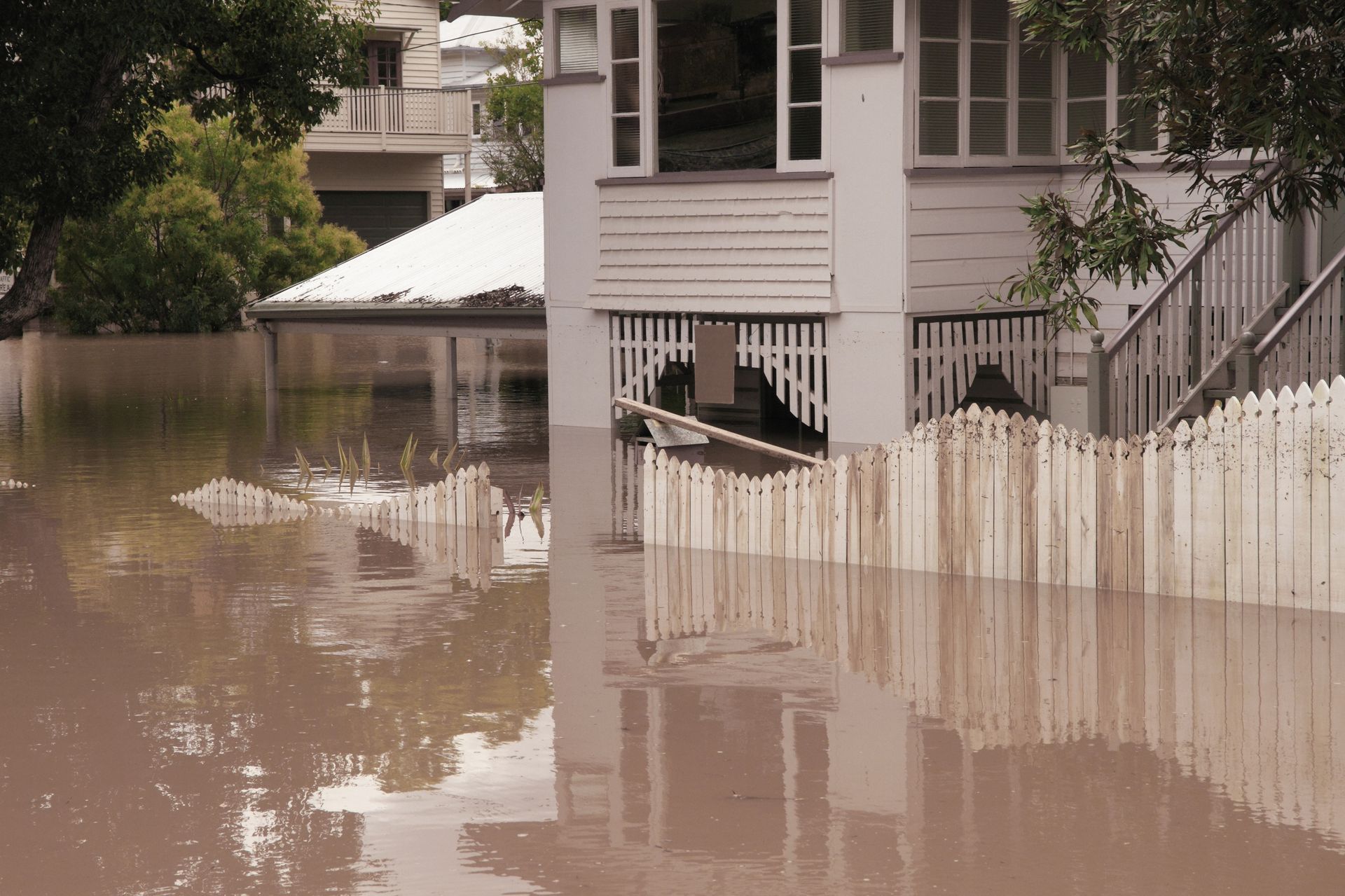 A flooded house with a white picket fence in front of it