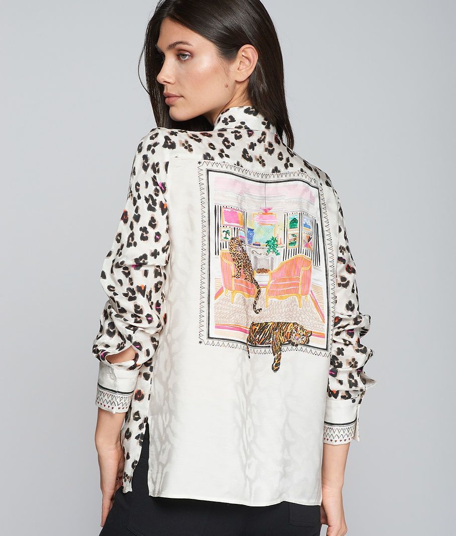 Woman wearing a white shirt with leopard print sleeves, a back panel with a printed cat scene.