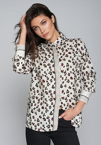 Woman in leopard print blouse and black pants, hand in pocket.