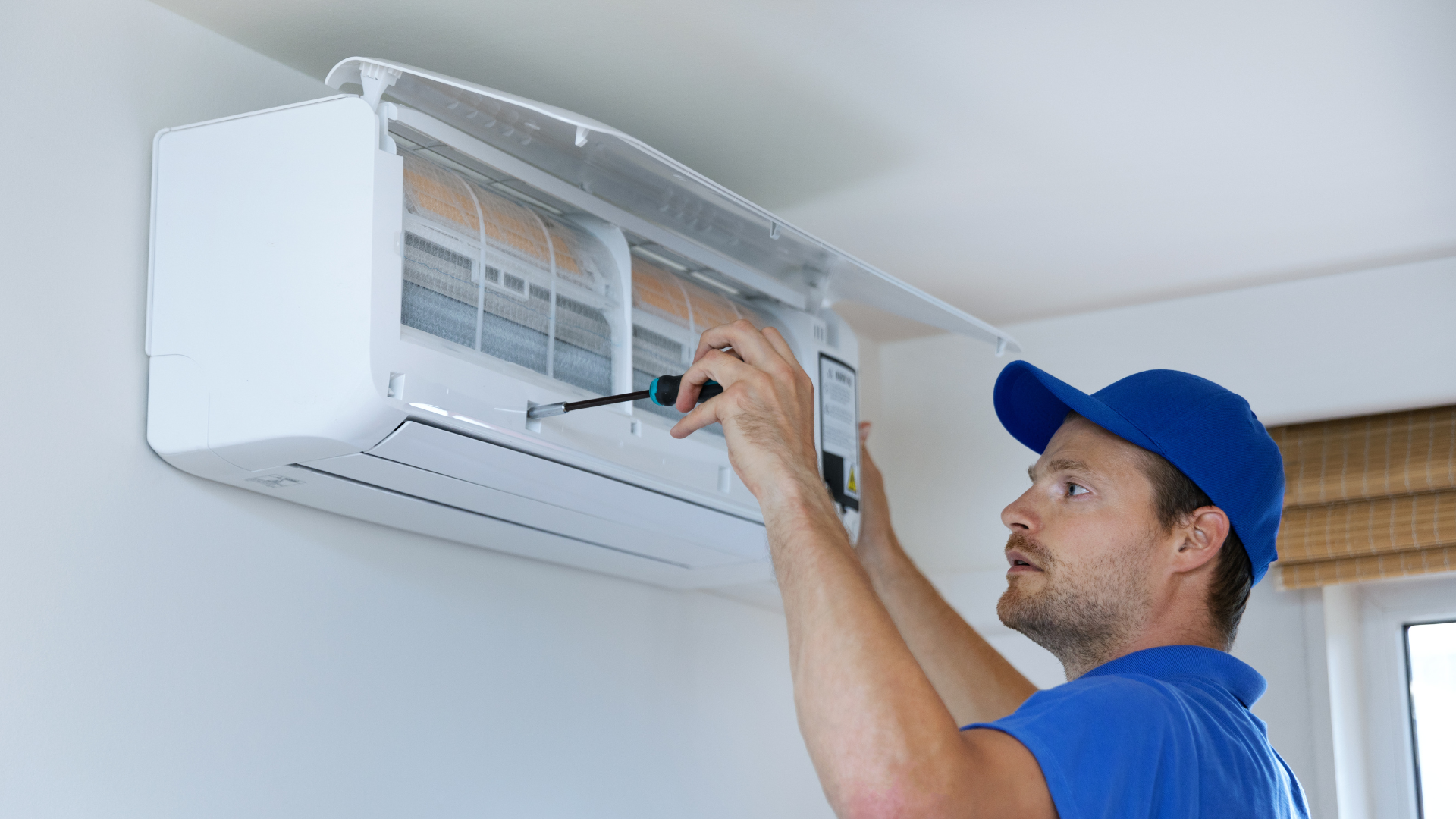A man is fixing an air conditioner with a screwdriver.