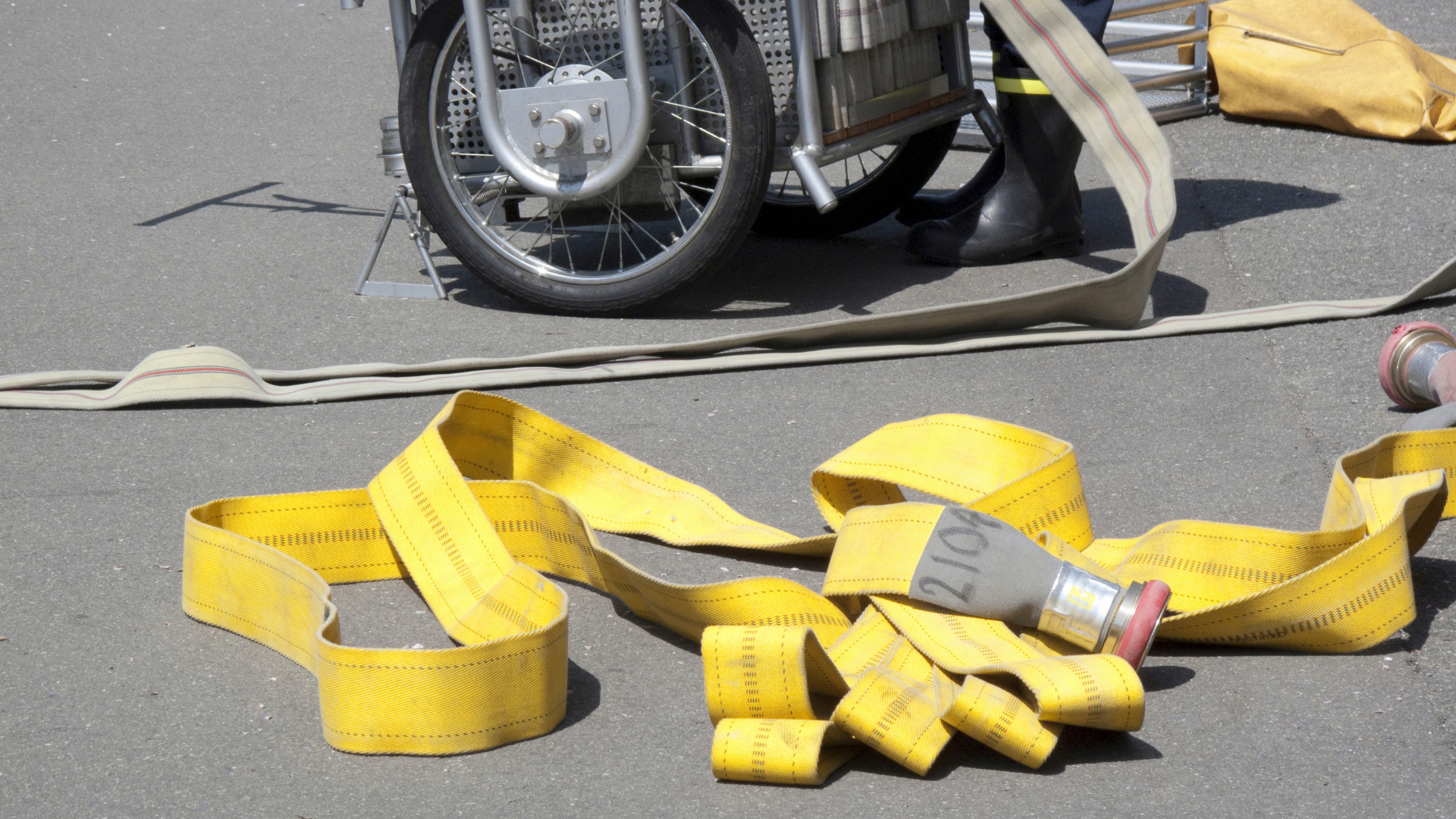A yellow hose is laying on the ground next to a motorcycle wheel