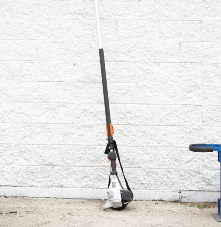 A lawn mower is leaning against a white brick wall