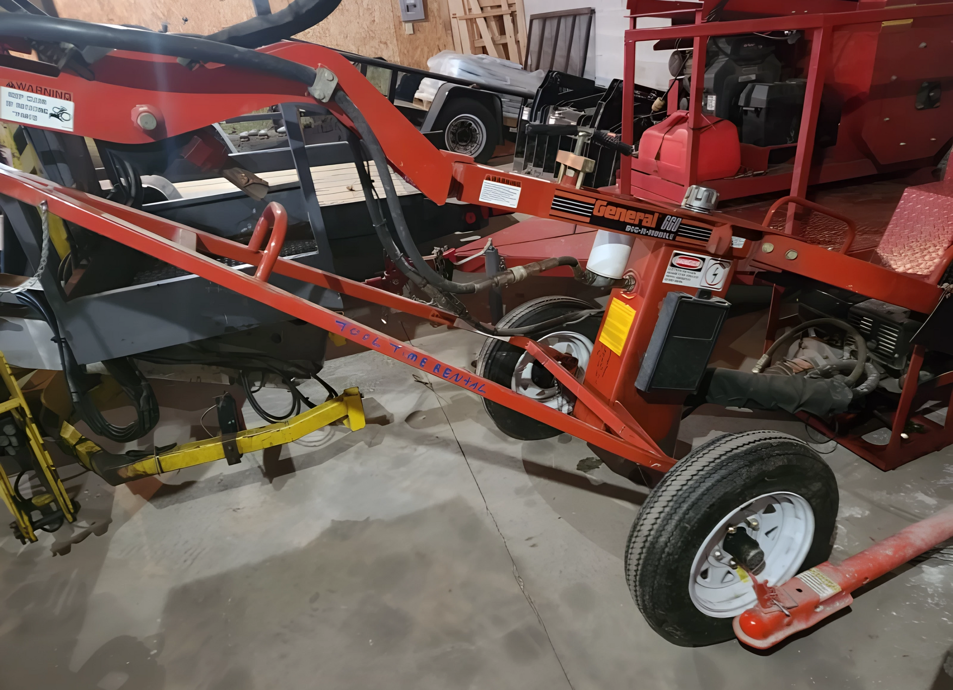 A red tractor is parked in a garage next to other tractors.