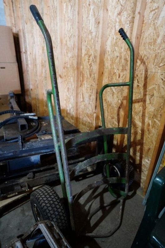 A green hand truck is sitting in a garage next to a wooden wall.