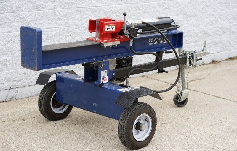 A blue log splitter with wheels is sitting on the sidewalk.