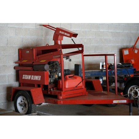 A red straw blower is on a trailer in a garage.