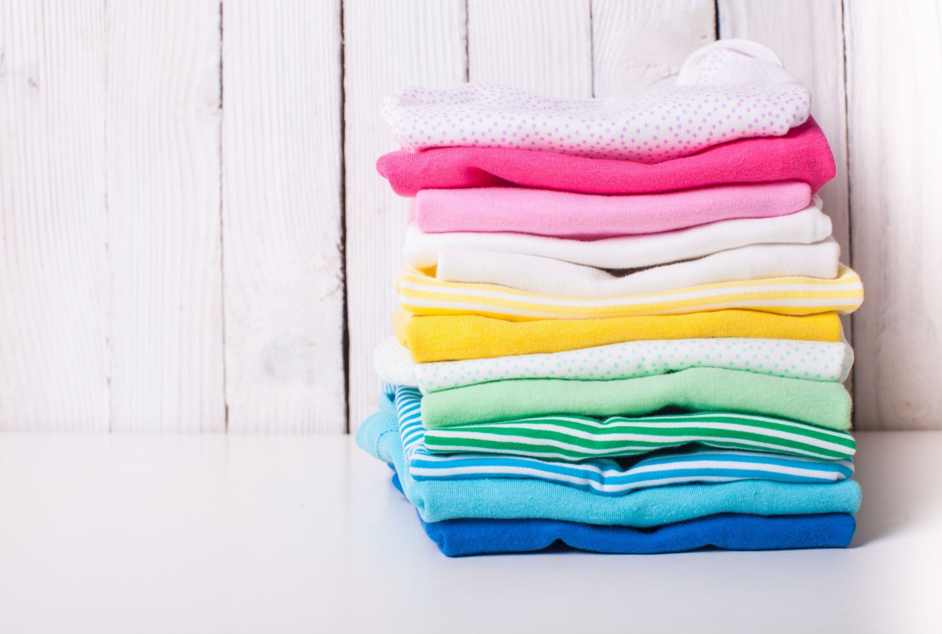 a stack of colorful baby clothes on a white table